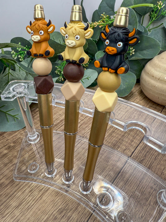 Three colorful pen holders with cartoon animal figures on top, placed on a wooden surface.