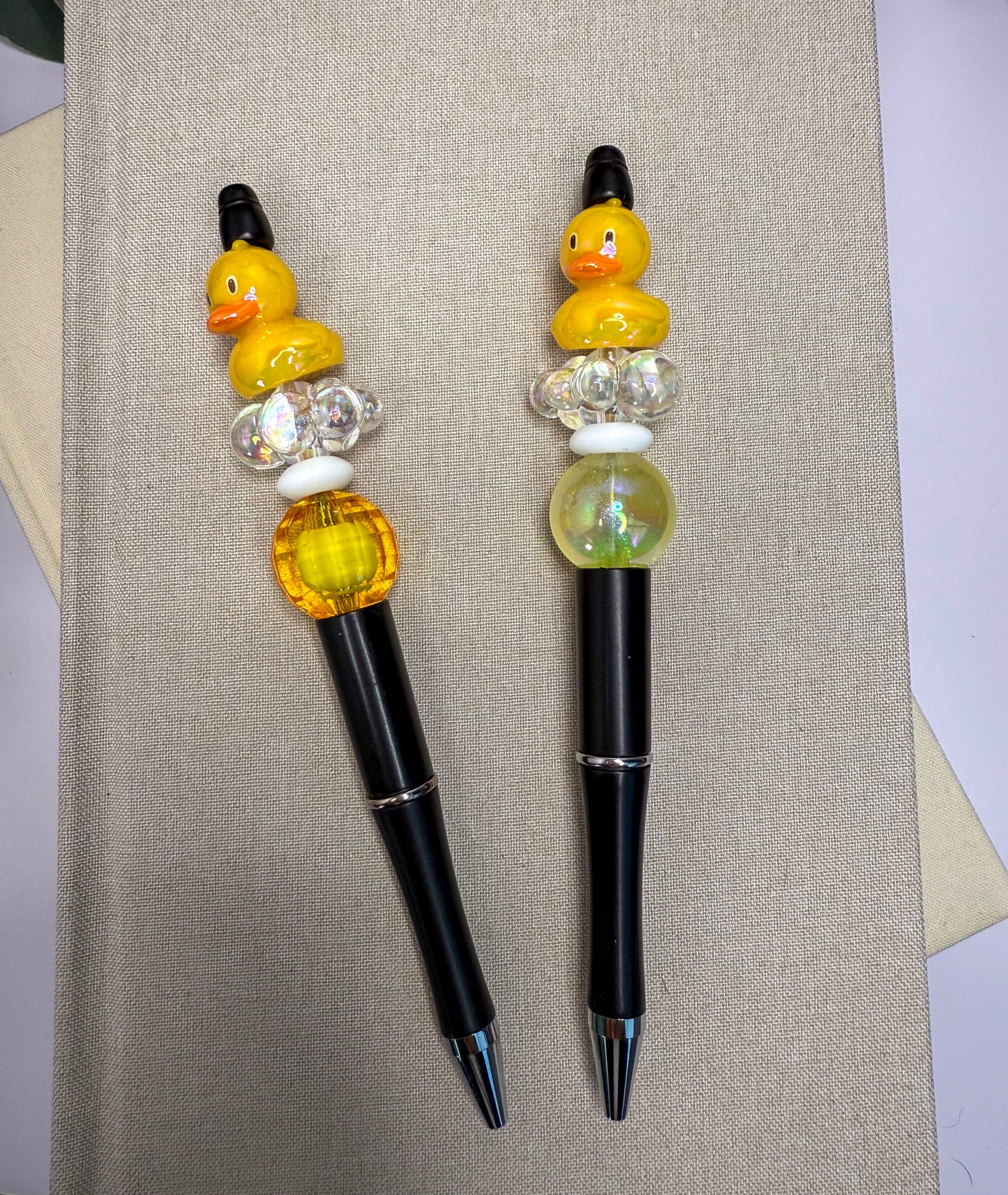 two pens with colorful beads on them, placed on a beige surface.