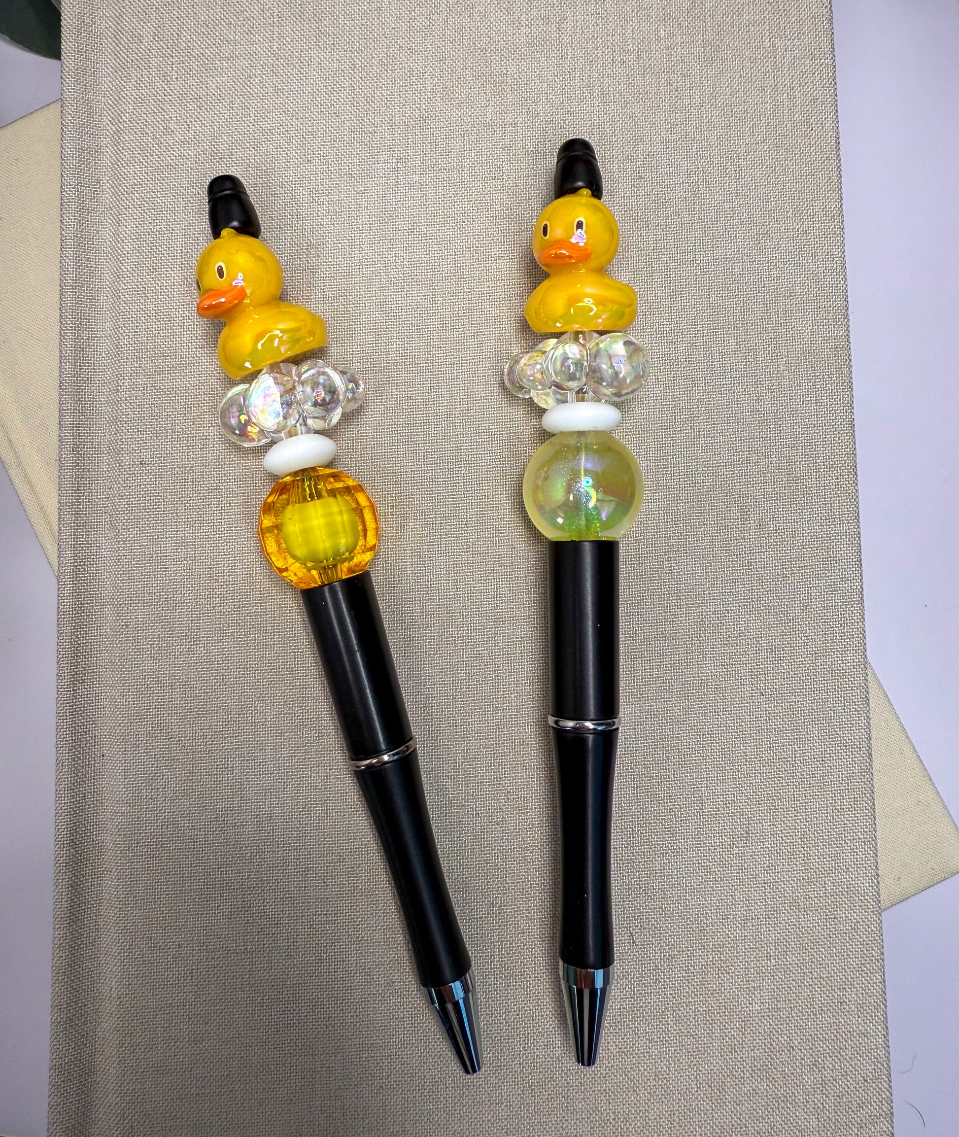 two pens with colorful beads on them, placed on a beige surface.
