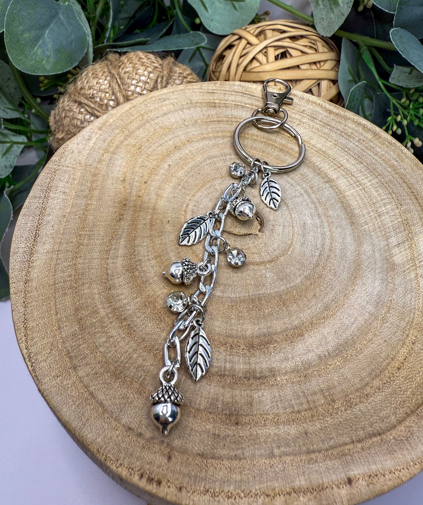 A silver keychain with a dangling charm featuring leaves and acorns, resting on a wooden surface.