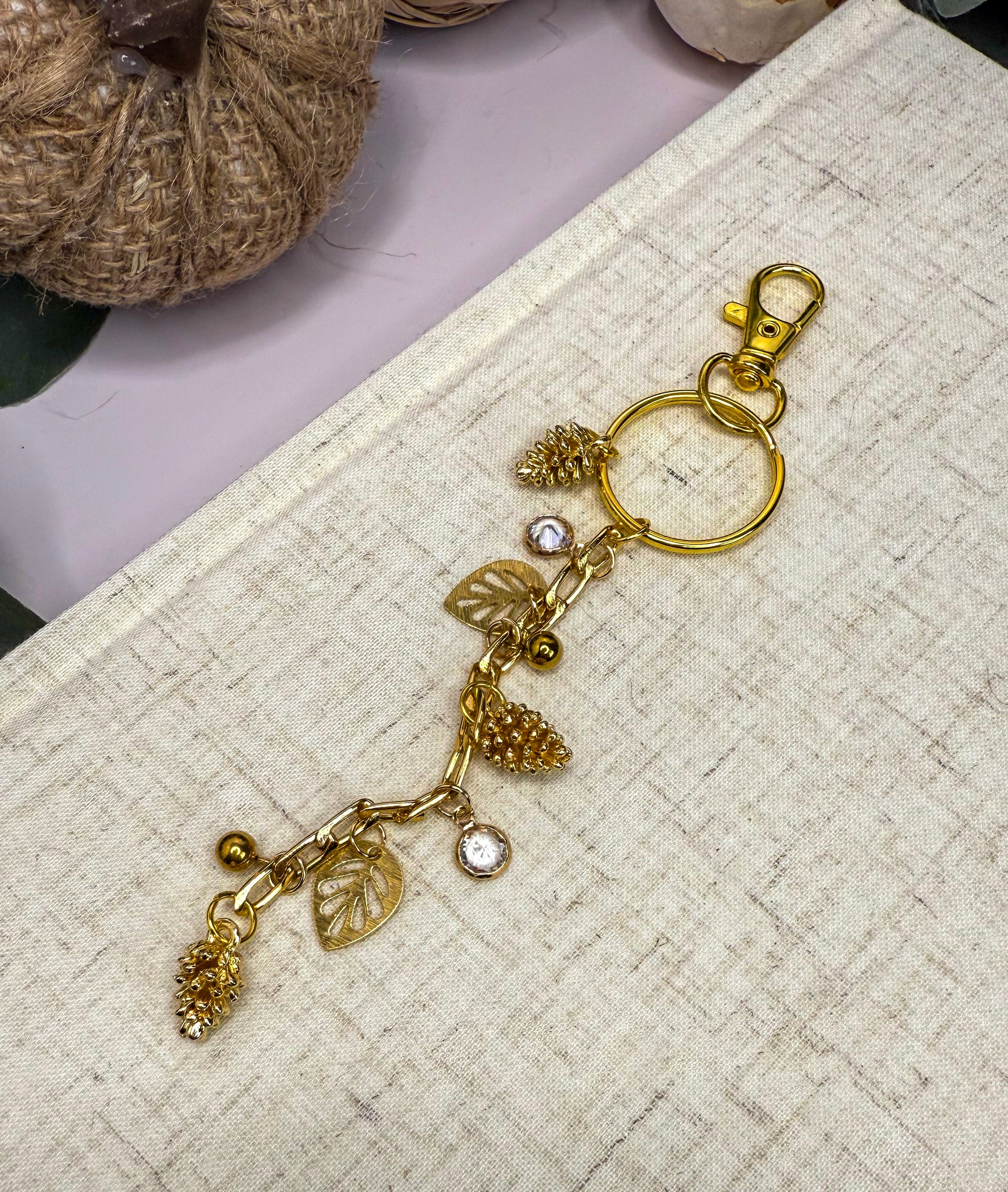 A gold-colored keychain with various charms, including pine cones and leaves, attached to a metal ring.
