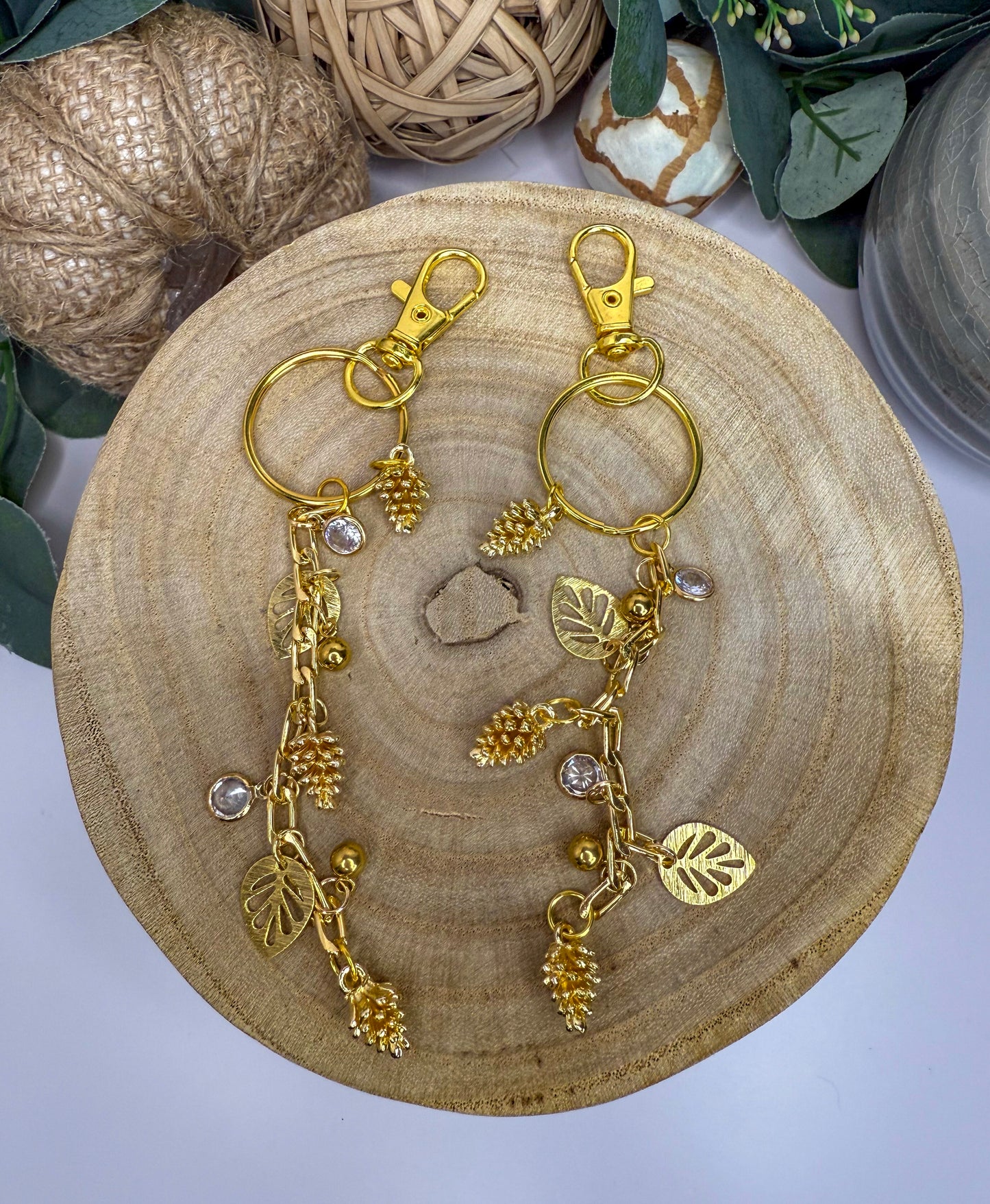 A pair of gold-colored keychains with leaf-shaped charms and small crystal pendants, displayed on a wooden surface.
