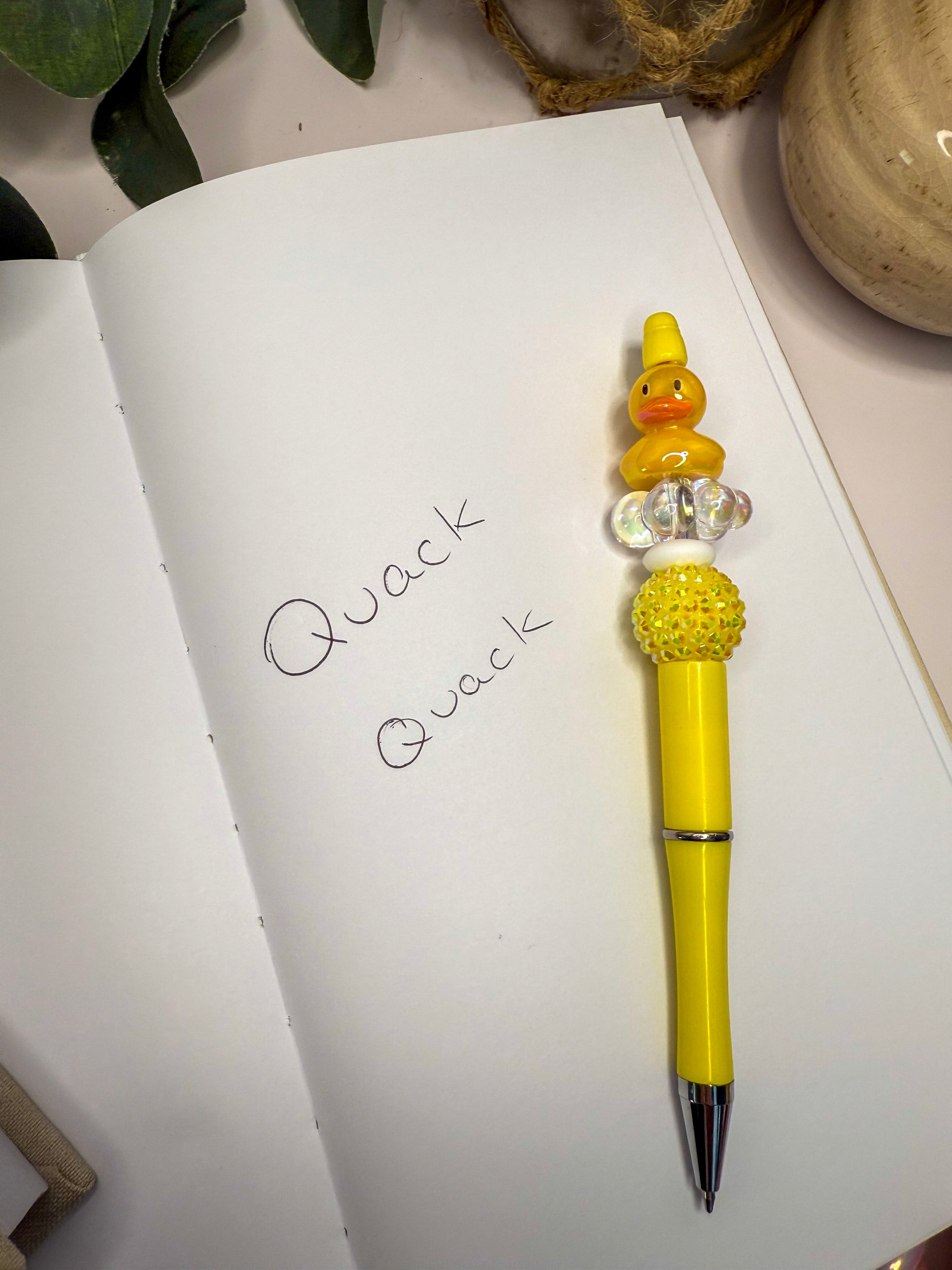 a yellow pen with a duck figurine on top of it, placed on a white notebook with the word "Quack" written on it.