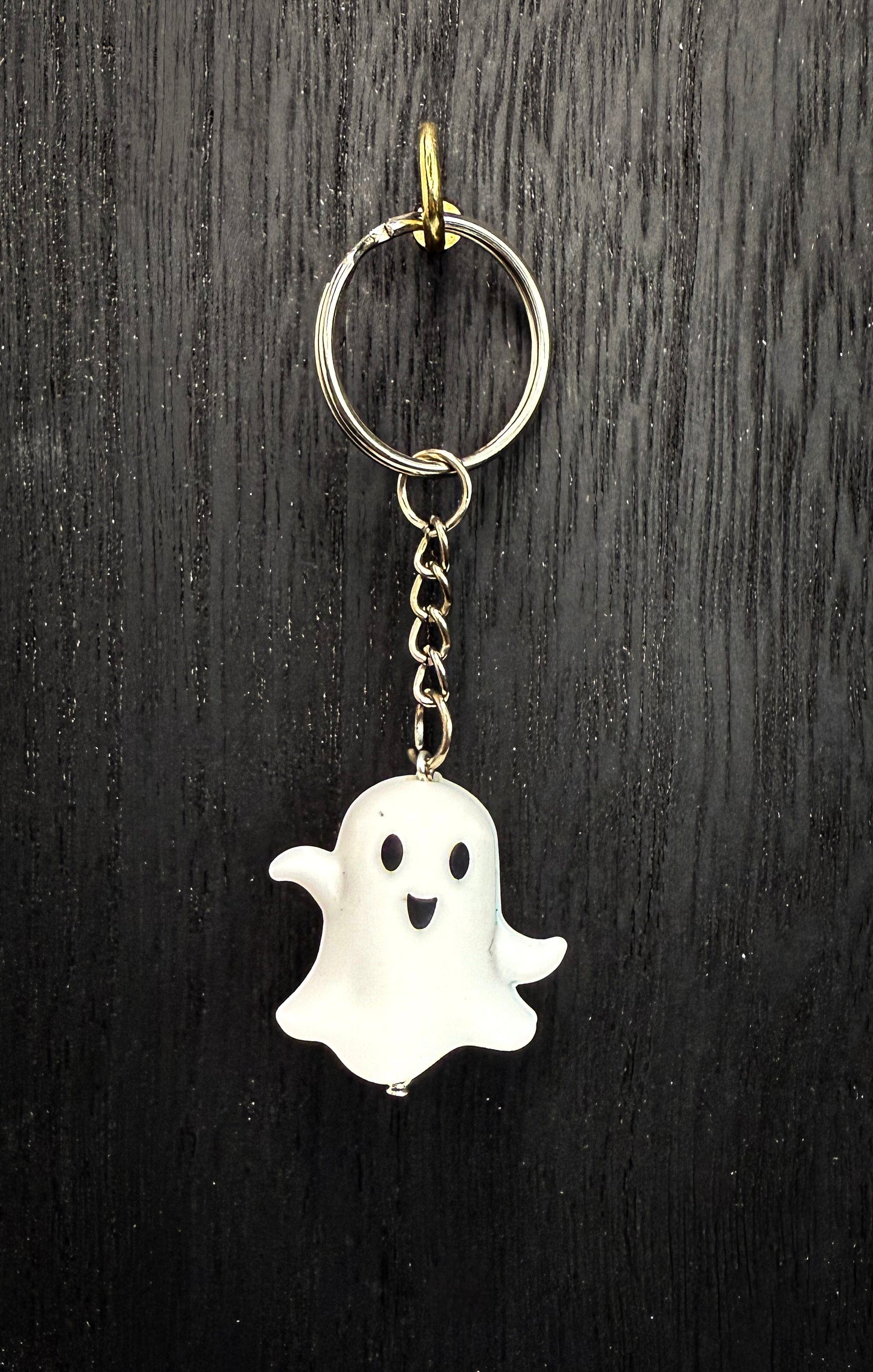 A keychain in the shape of a ghost with a smiling face, hanging from a chain on a dark wooden surface.