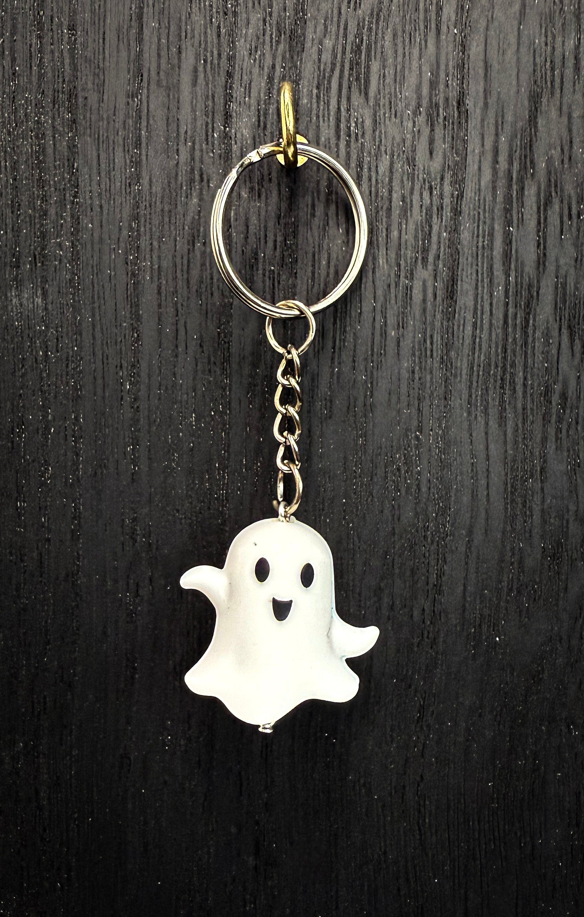 A keychain in the shape of a ghost with a smiling face, hanging from a chain on a dark wooden surface.