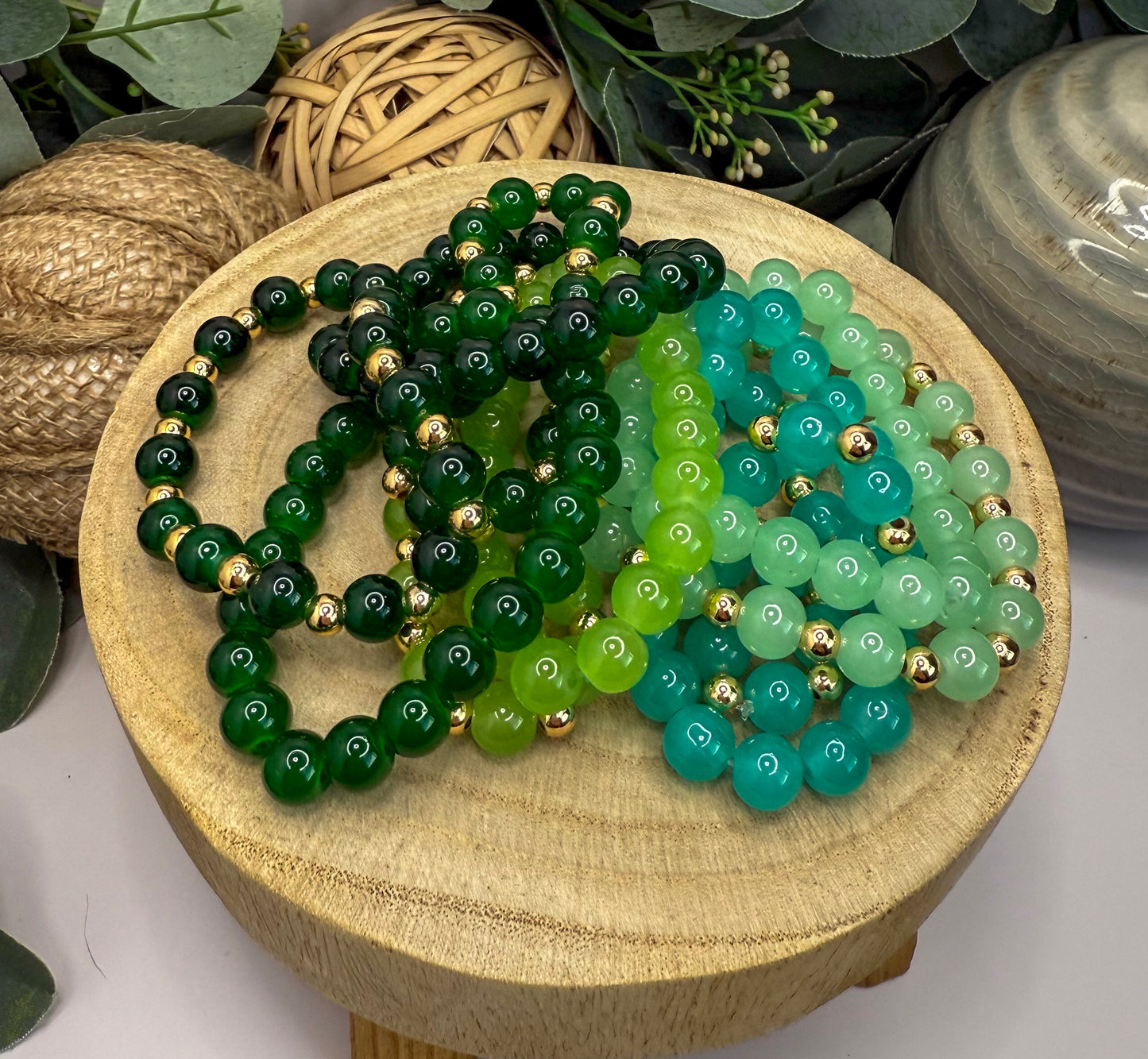 A wooden stand displays a collection of colorful beaded bracelets, including green and turquoise beads, arranged in a visually appealing manner.