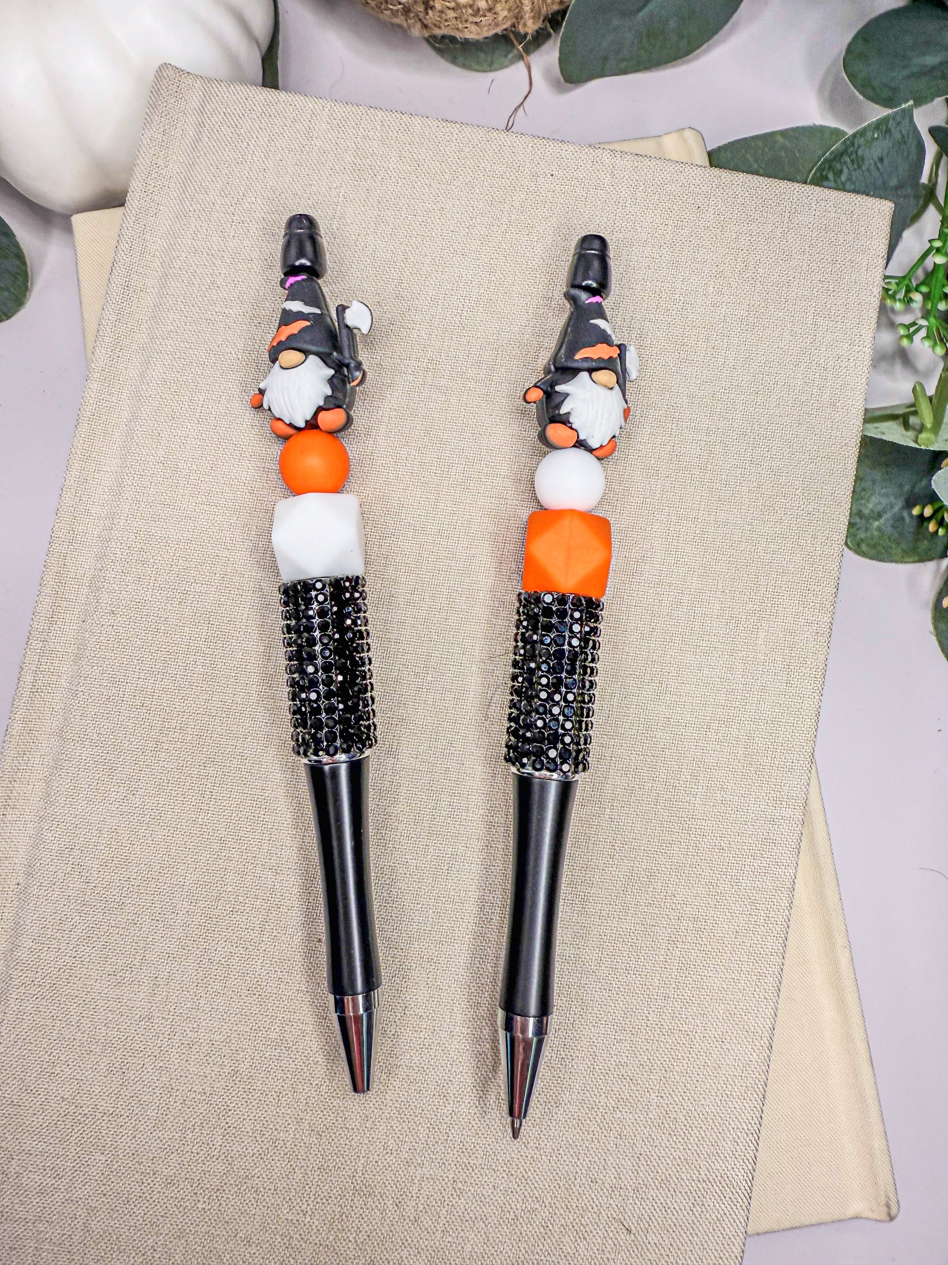two ornate pens with black and orange embellishments, placed on a beige surface.