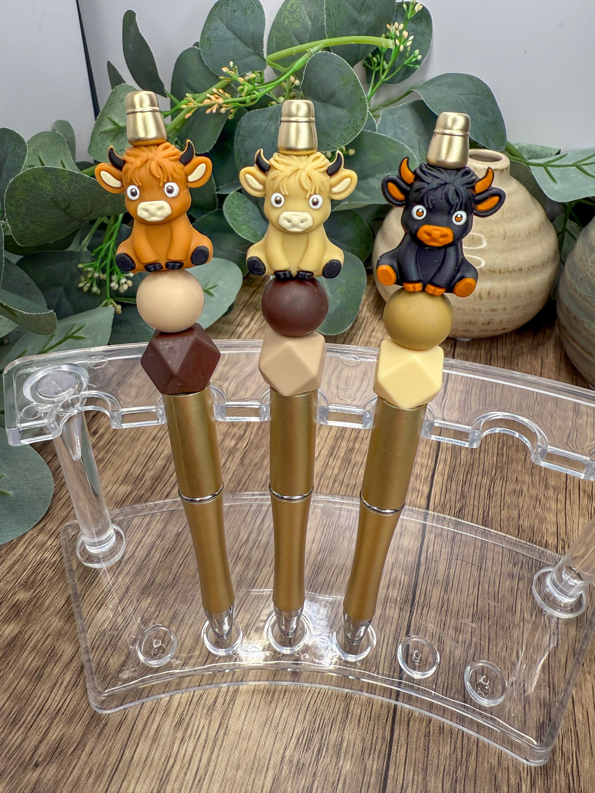 Three colorful pen holders with animal figurines on top, placed on a wooden surface.