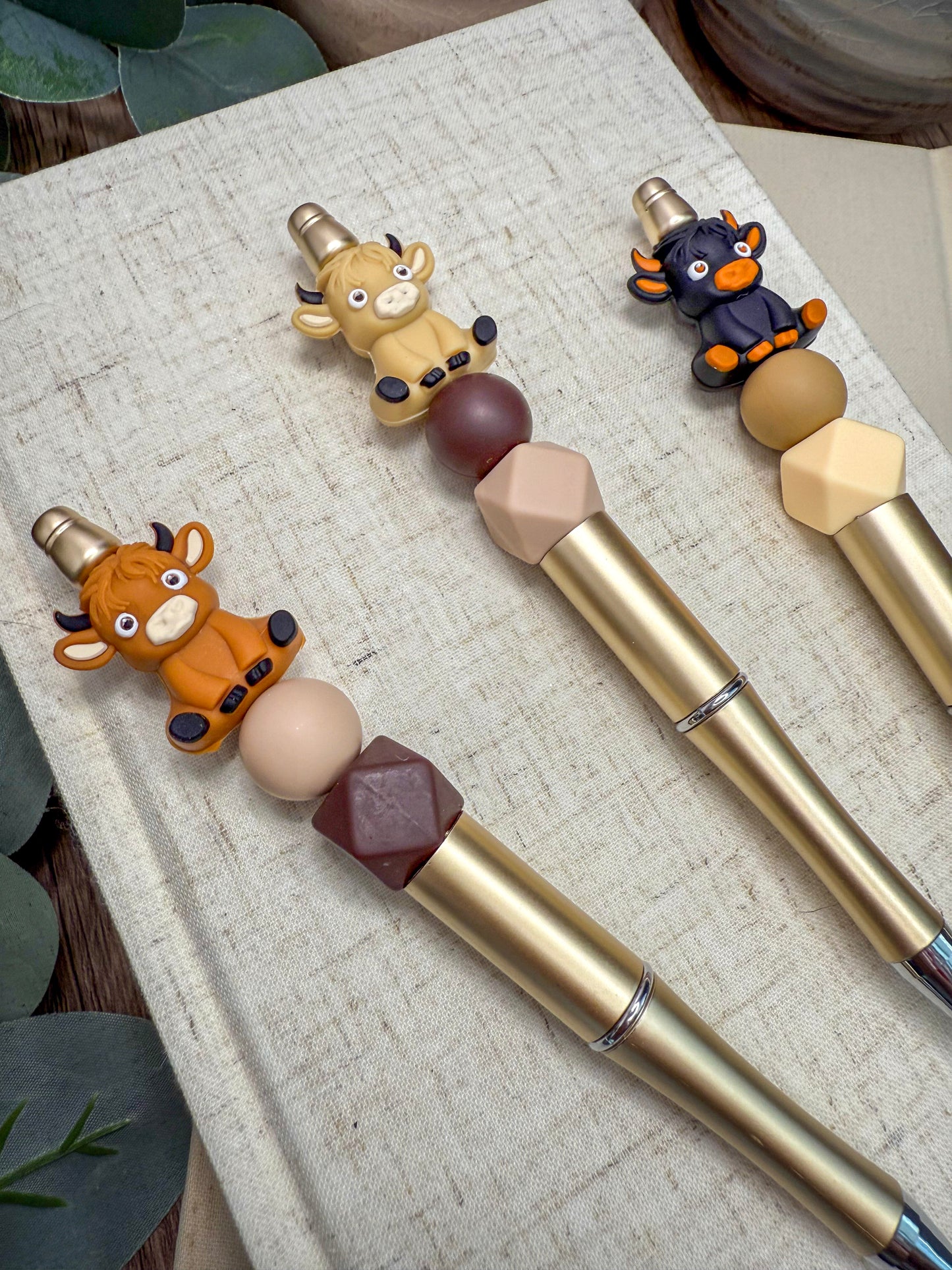three pens with animal-themed decorations, including a cow, a bull, and a cow, attached to the tips.