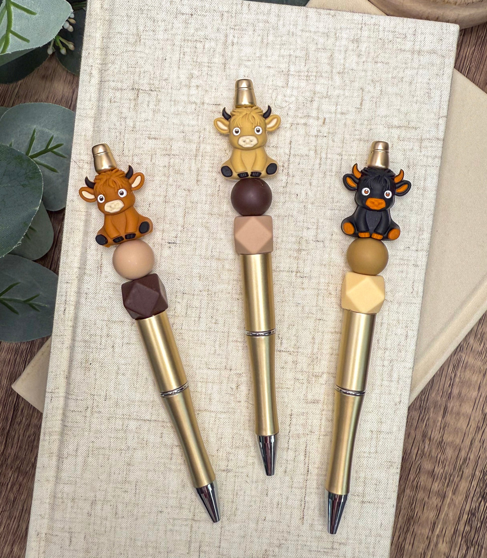 Three colorful pens with animal figurines attached to the tips are placed on a white surface.