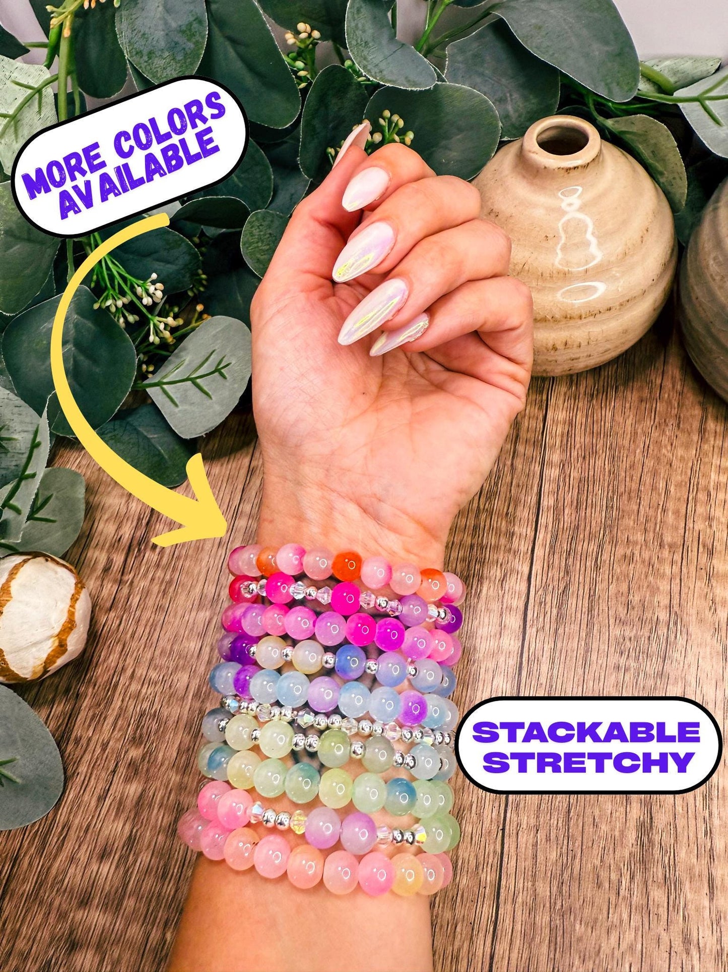 A person's hand wearing a stackable stretchy bracelet, with a sign indicating that there are more colors available.
