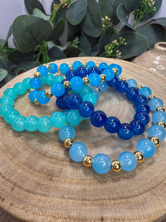 A collection of colorful beaded bracelets arranged on a wooden surface, with a backdrop of greenery.