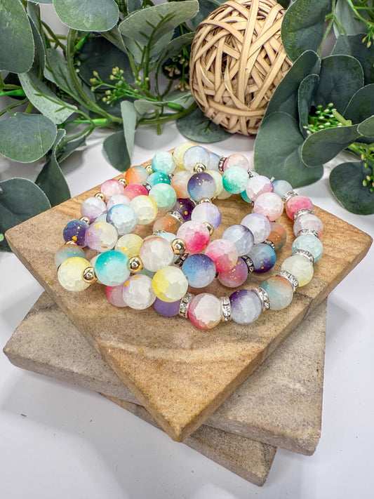 A collection of multicolored beaded bracelets arranged on a wooden surface, with a woven basket and greenery in the background.