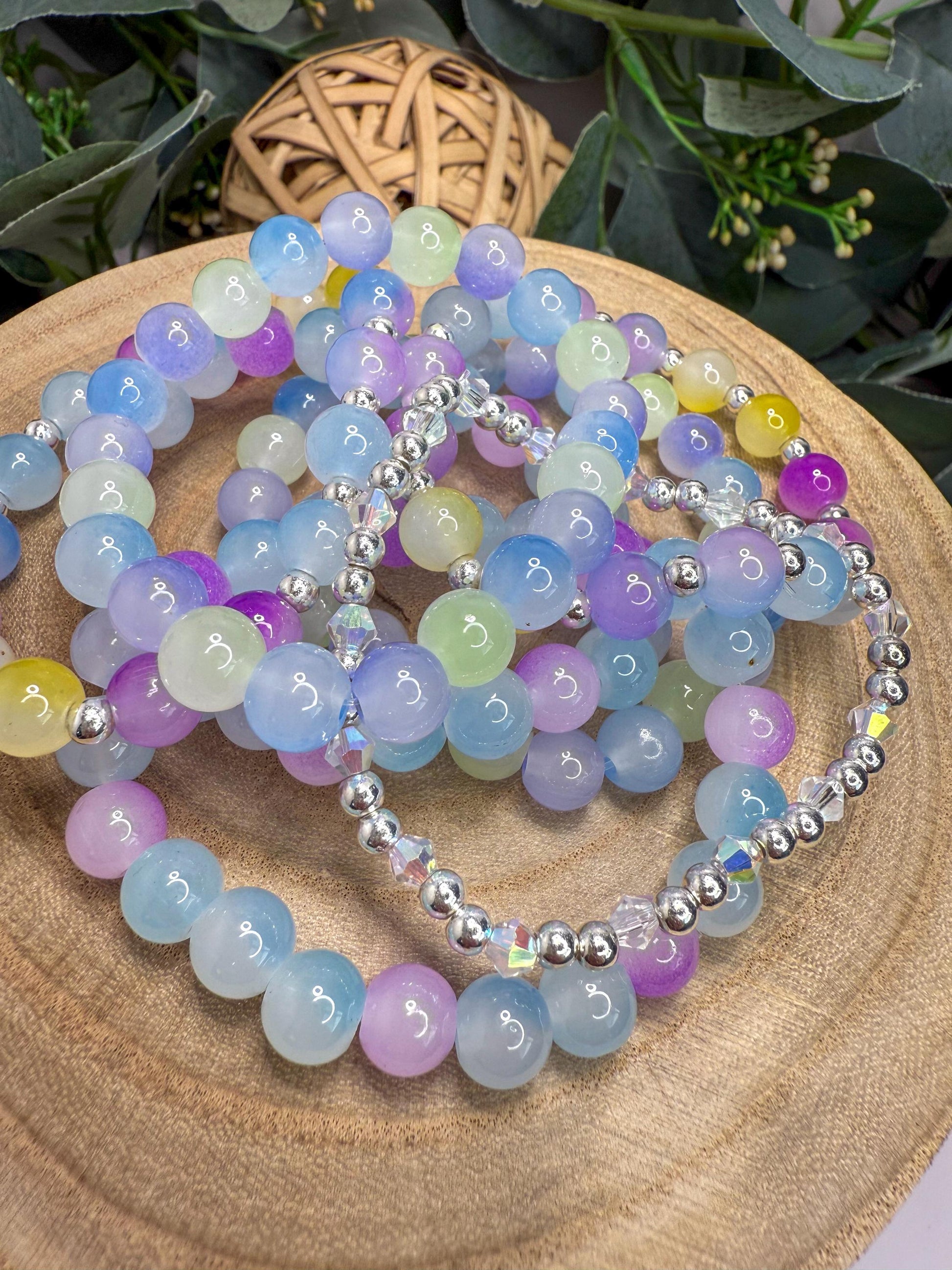 A collection of colorful beaded bracelets arranged on a wooden surface, with a woven basket and greenery in the background.