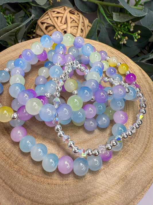 A collection of colorful beaded bracelets arranged on a wooden surface, with a woven basket and greenery in the background.