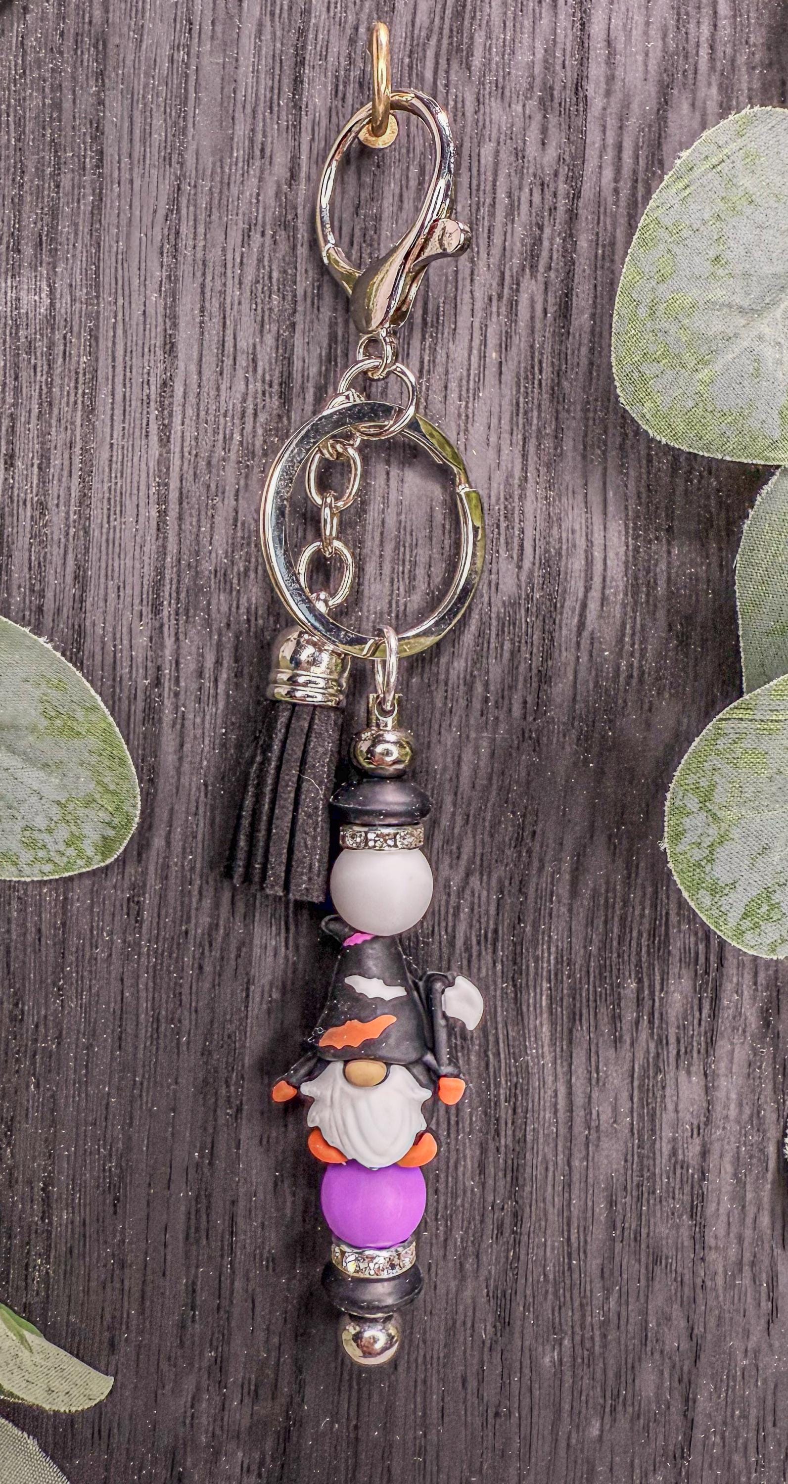 A keychain with a gnome-like figure and various beads or charms attached to it, hanging on a hook against a wooden background.