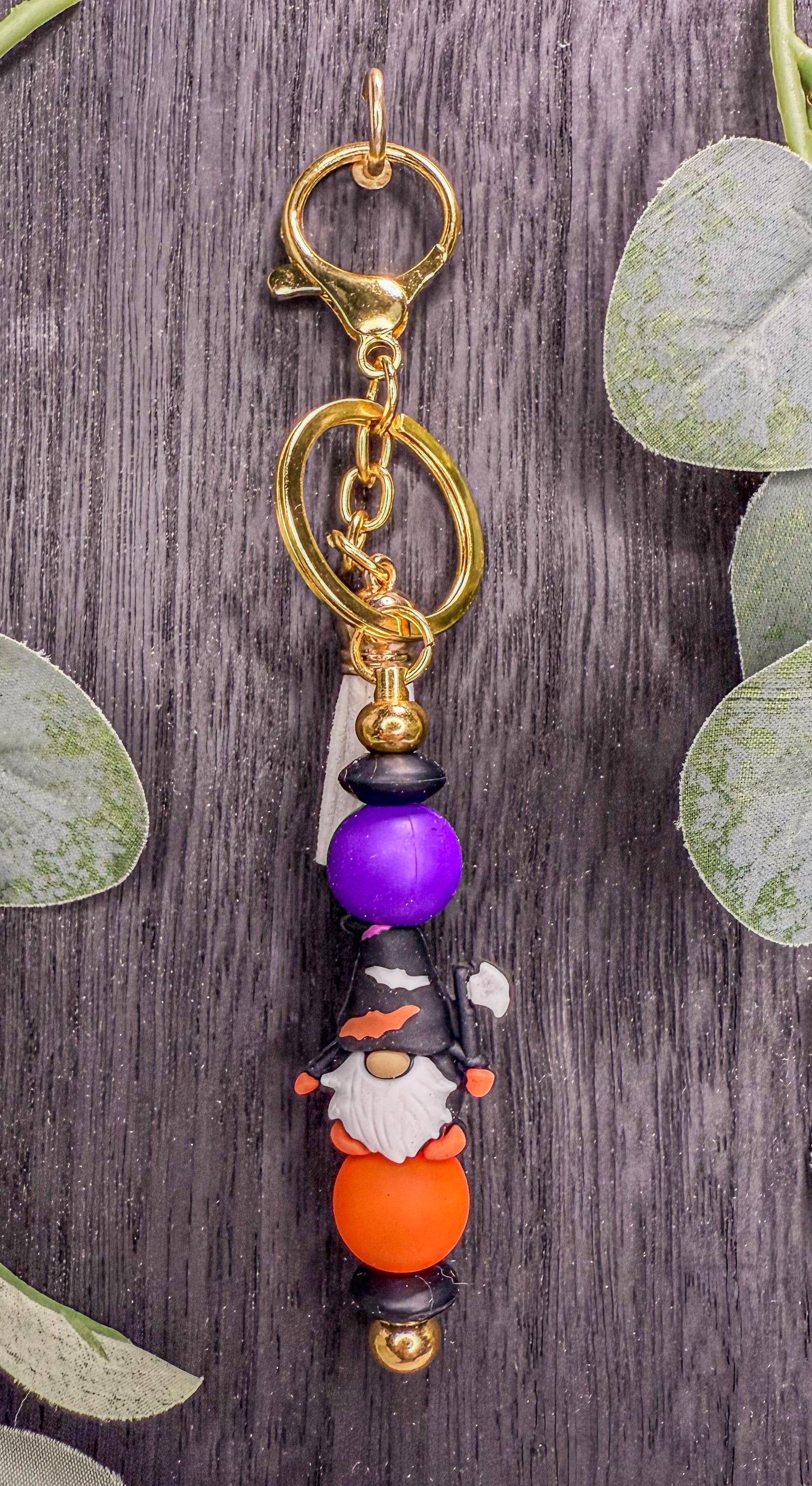A colorful keychain with a gnome design, featuring a purple bead, an orange bead, and a gold-colored charm.