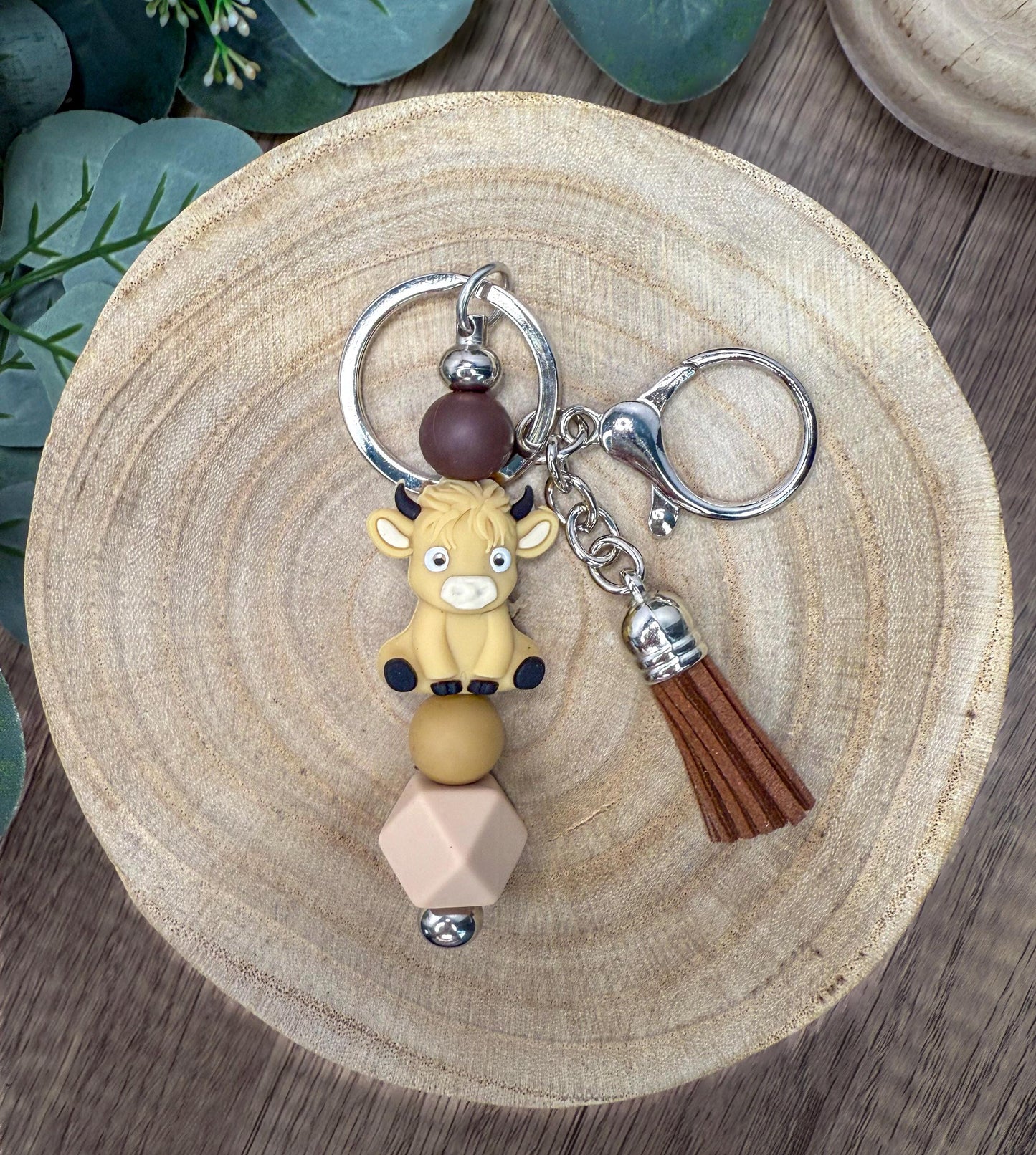 A keychain featuring a cartoon character, likely a cow, with a tassel attached, resting on a wooden surface.