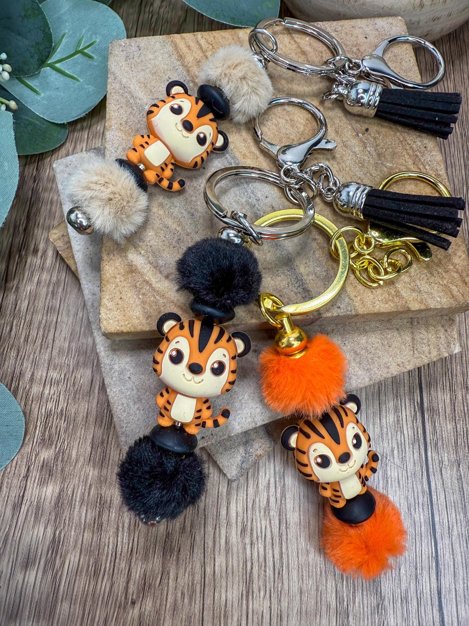 A collection of colorful keychains featuring cartoon tiger designs, including a black and orange tiger with pom poms.