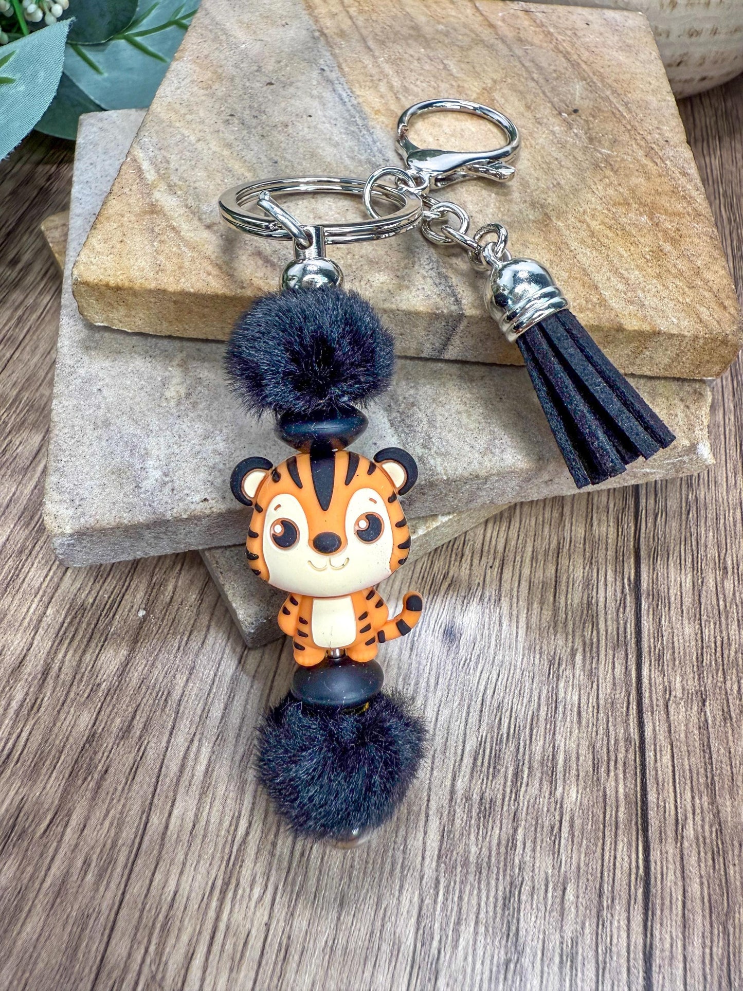A keychain featuring a cartoon tiger character with a fluffy pom pom on top.