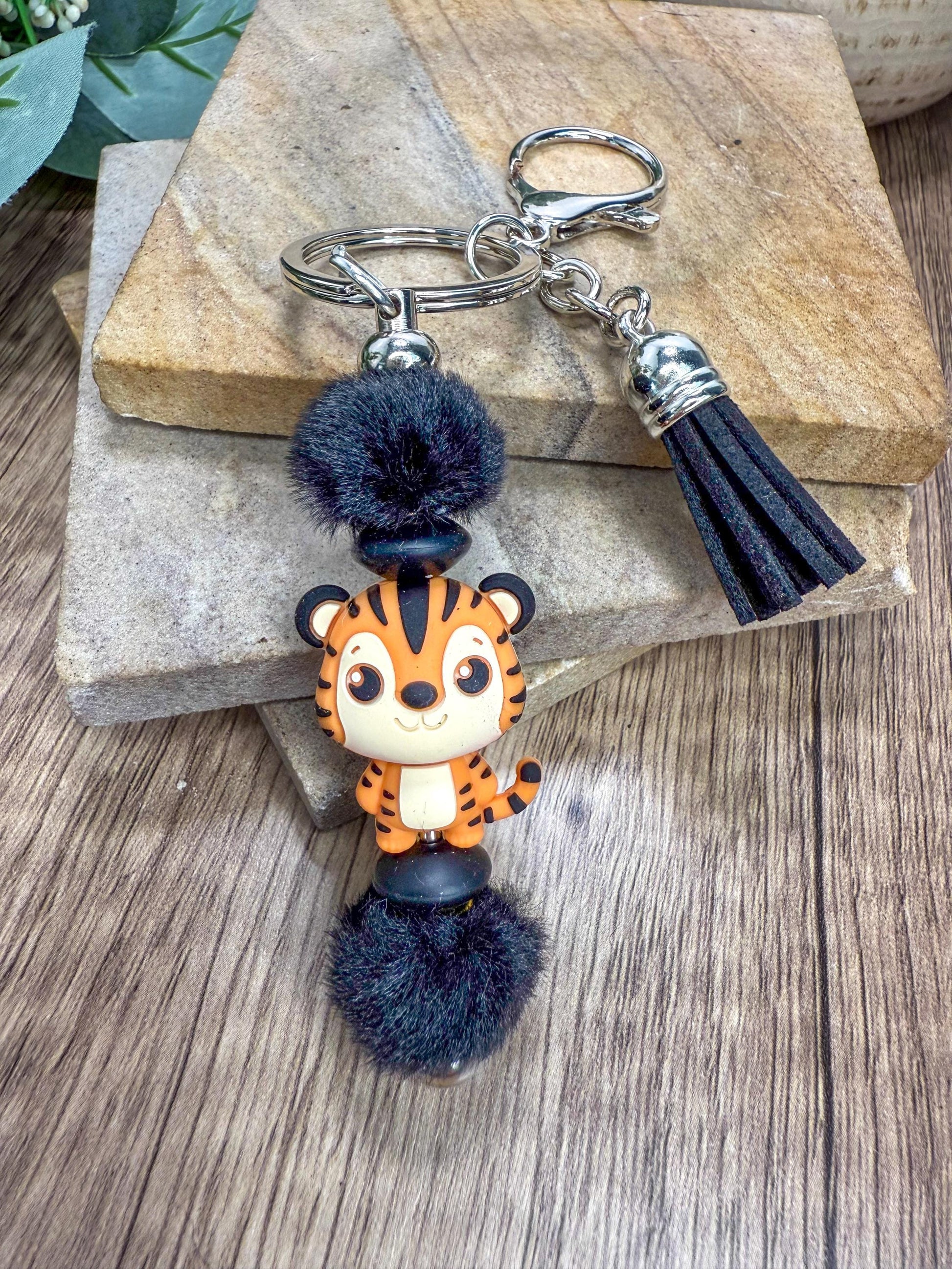 A keychain featuring a cartoon tiger character with a fluffy pom pom on top.