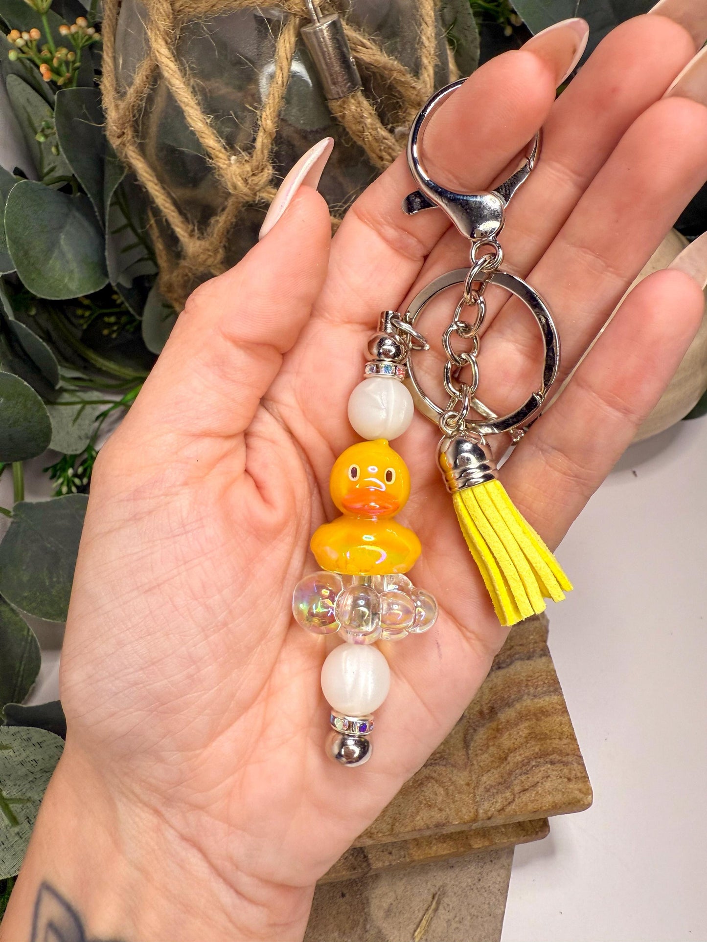 A hand holding a keychain with a yellow duck charm and beaded accents.