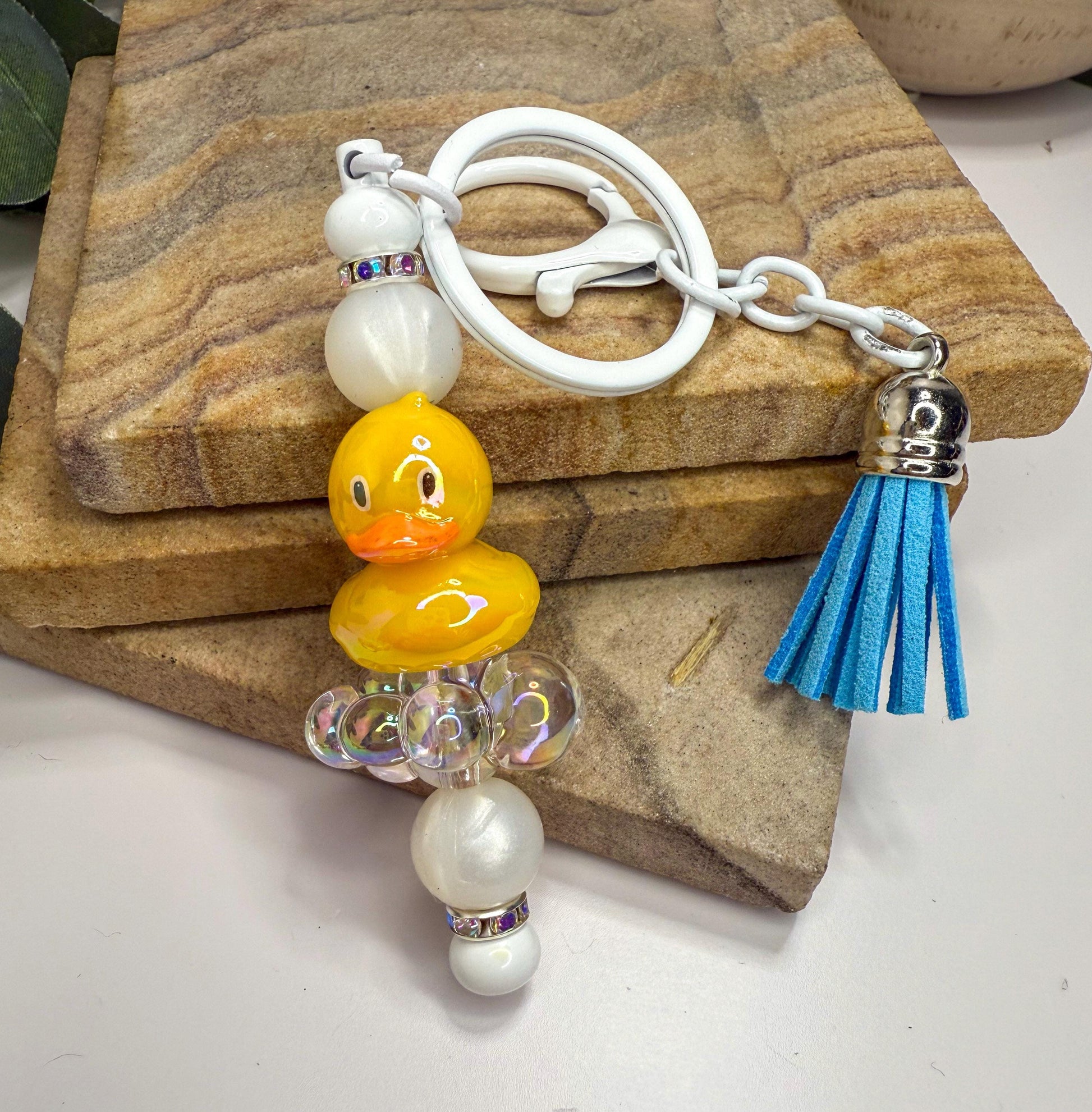 A keychain with a yellow duck charm and beaded accents, including white and blue tassels.