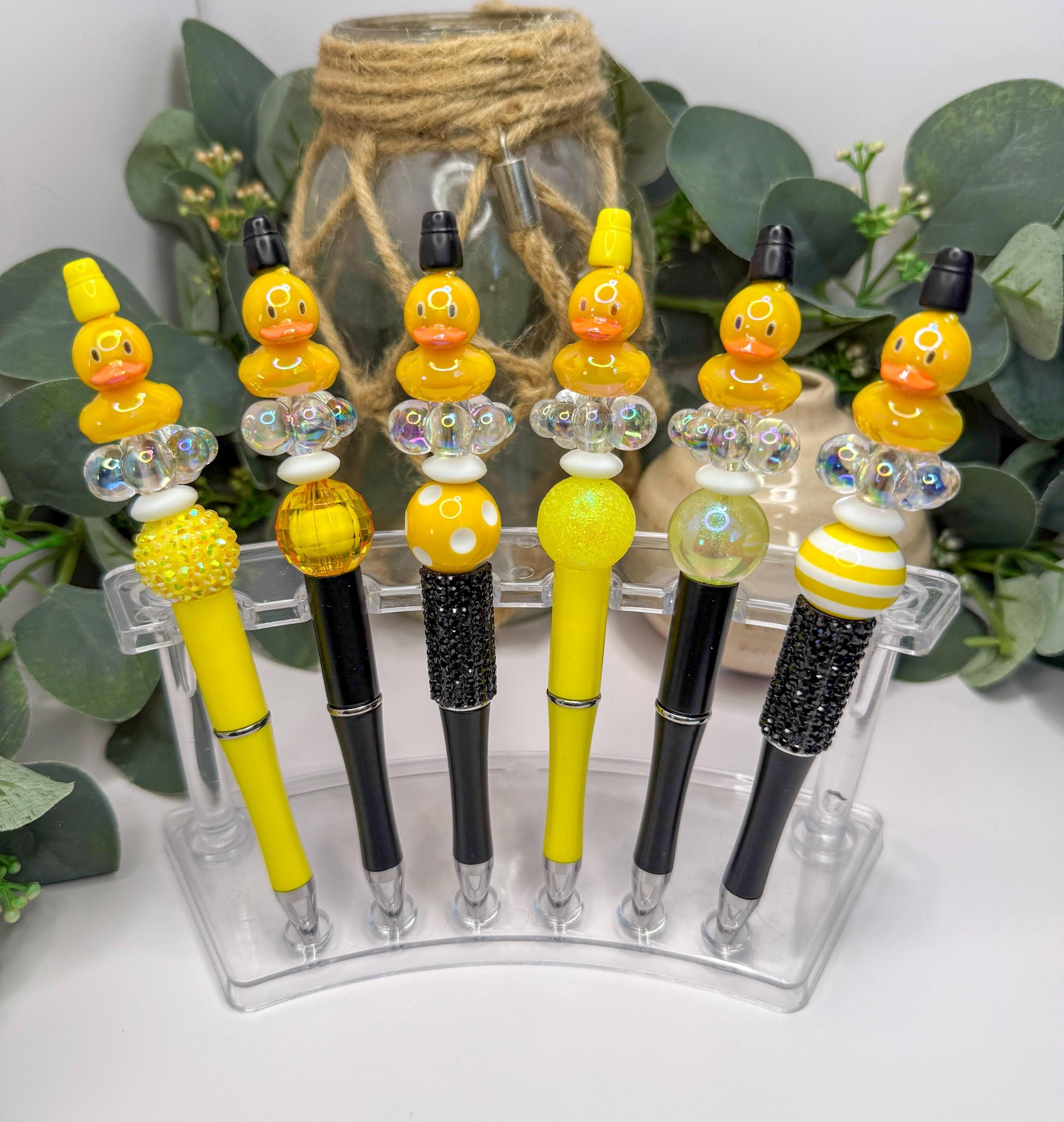 A collection of yellow and black pens with various decorative elements, such as beads and feathers, displayed on a clear stand.