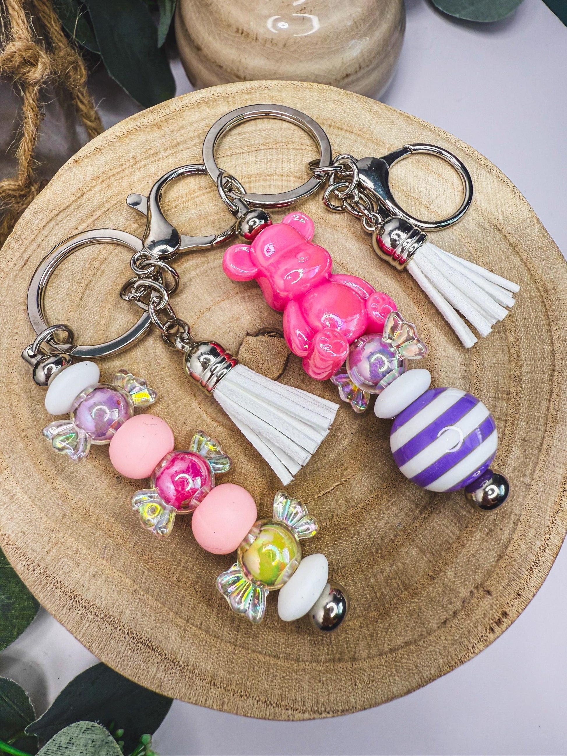 A collection of colorful keychains with various shapes and designs, including a pink bear keychain, a striped keychain, and a beaded keychain.