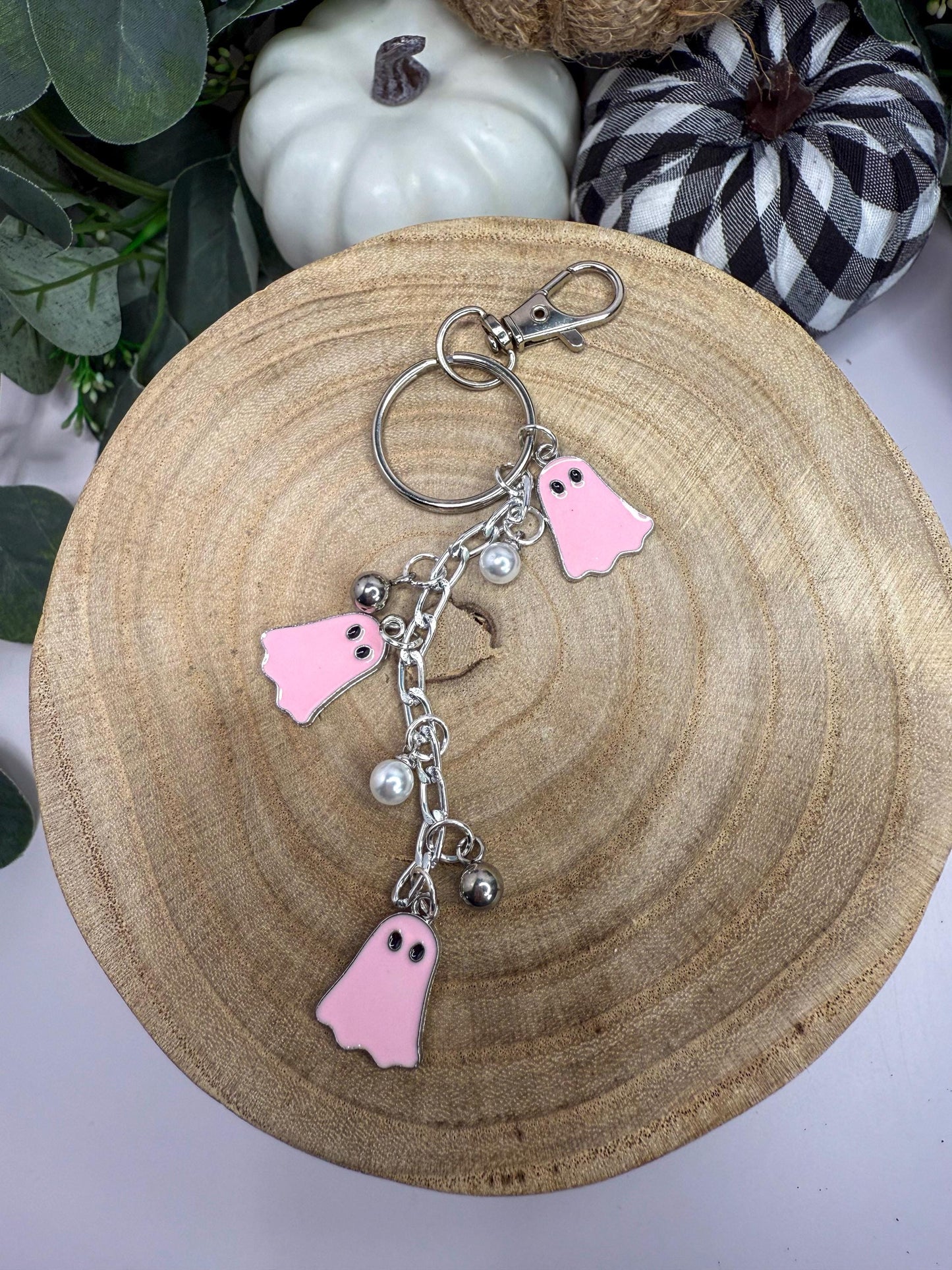 A wooden tray with a keychain featuring three pink ghost-shaped charms and silver bells.