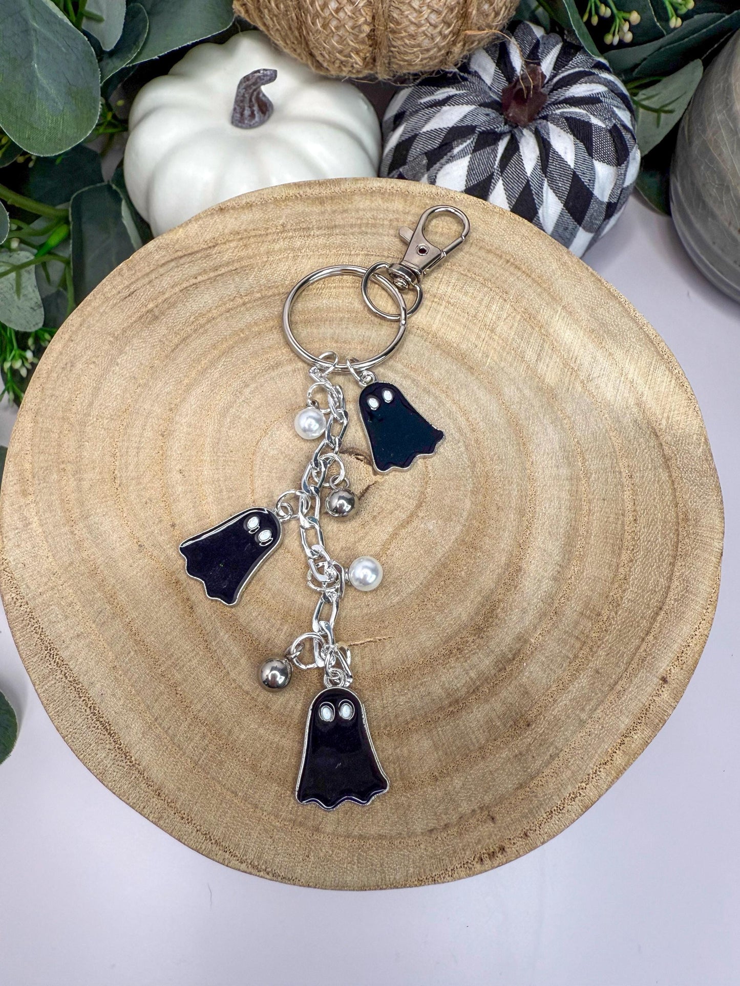 A wooden tray with a keychain featuring three black ghost-shaped charms and silver bells.