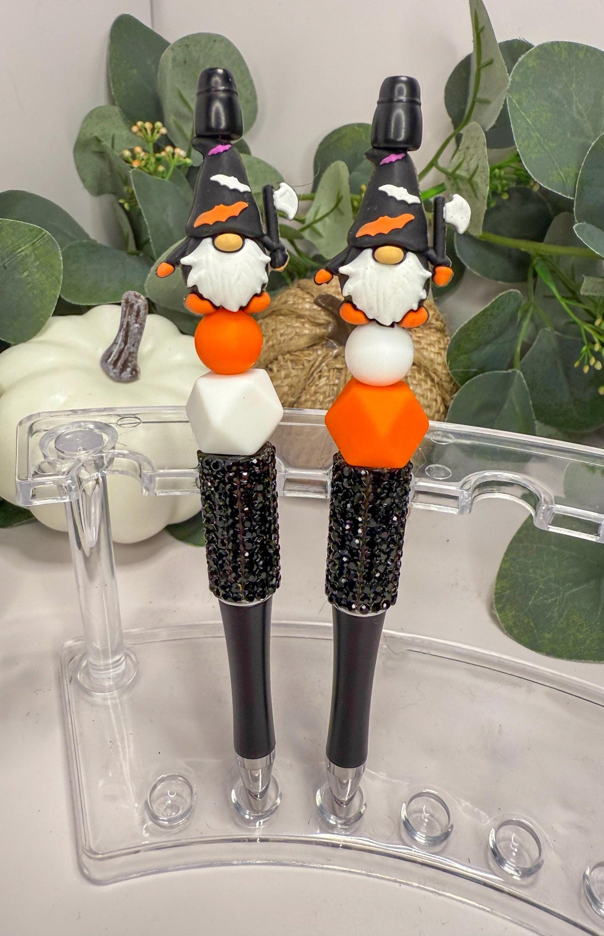 two gnome-themed pens with black and orange accents, placed on a clear stand.
