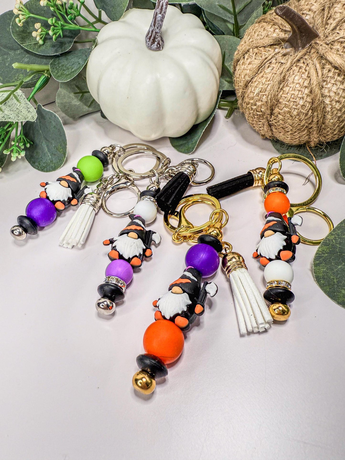 a collection of colorful keychains with various shapes and designs, including gnomes and beads, arranged on a white surface.