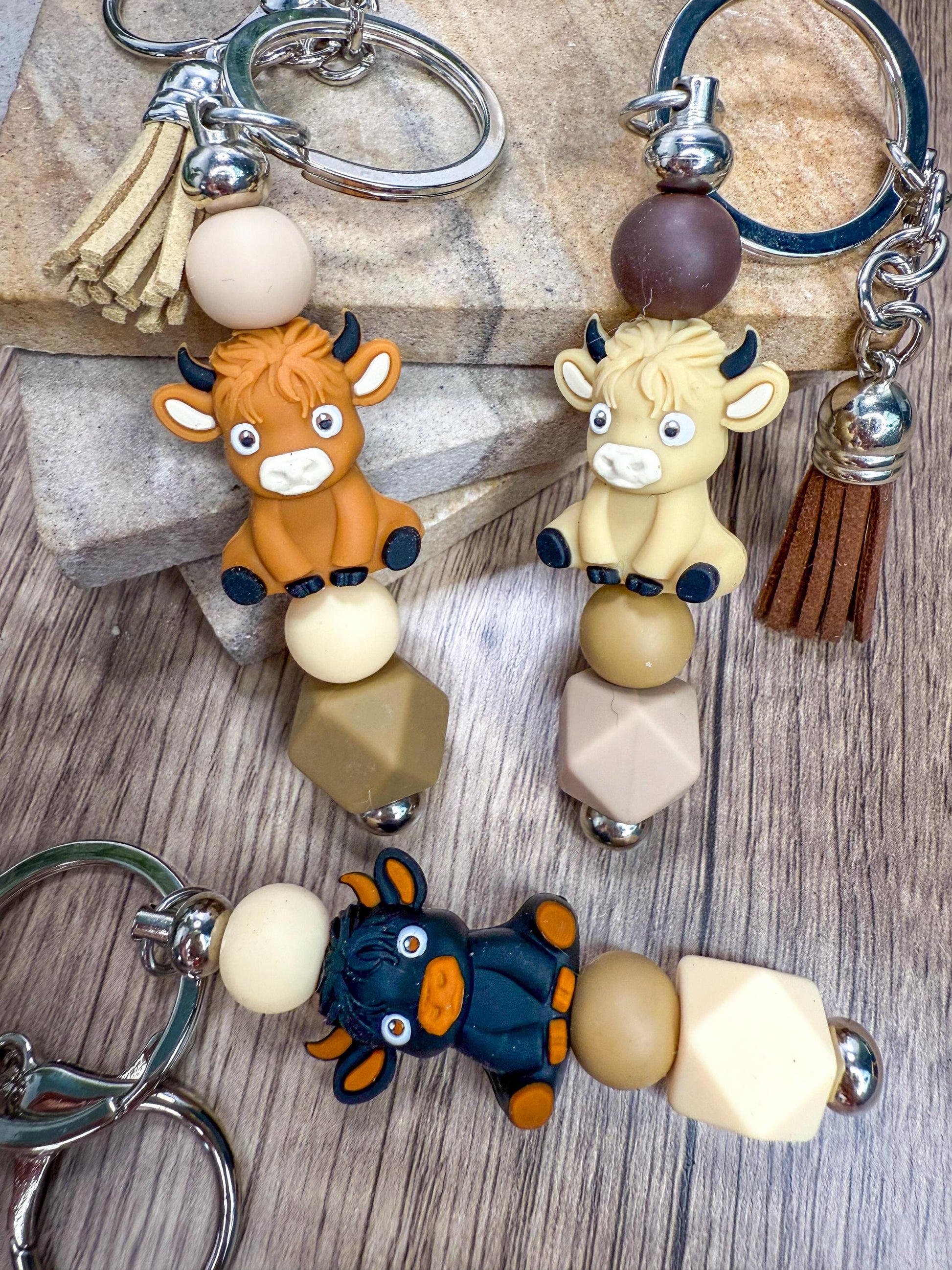 a collection of keychains with animal designs, including cows and bulls, arranged on a wooden surface.