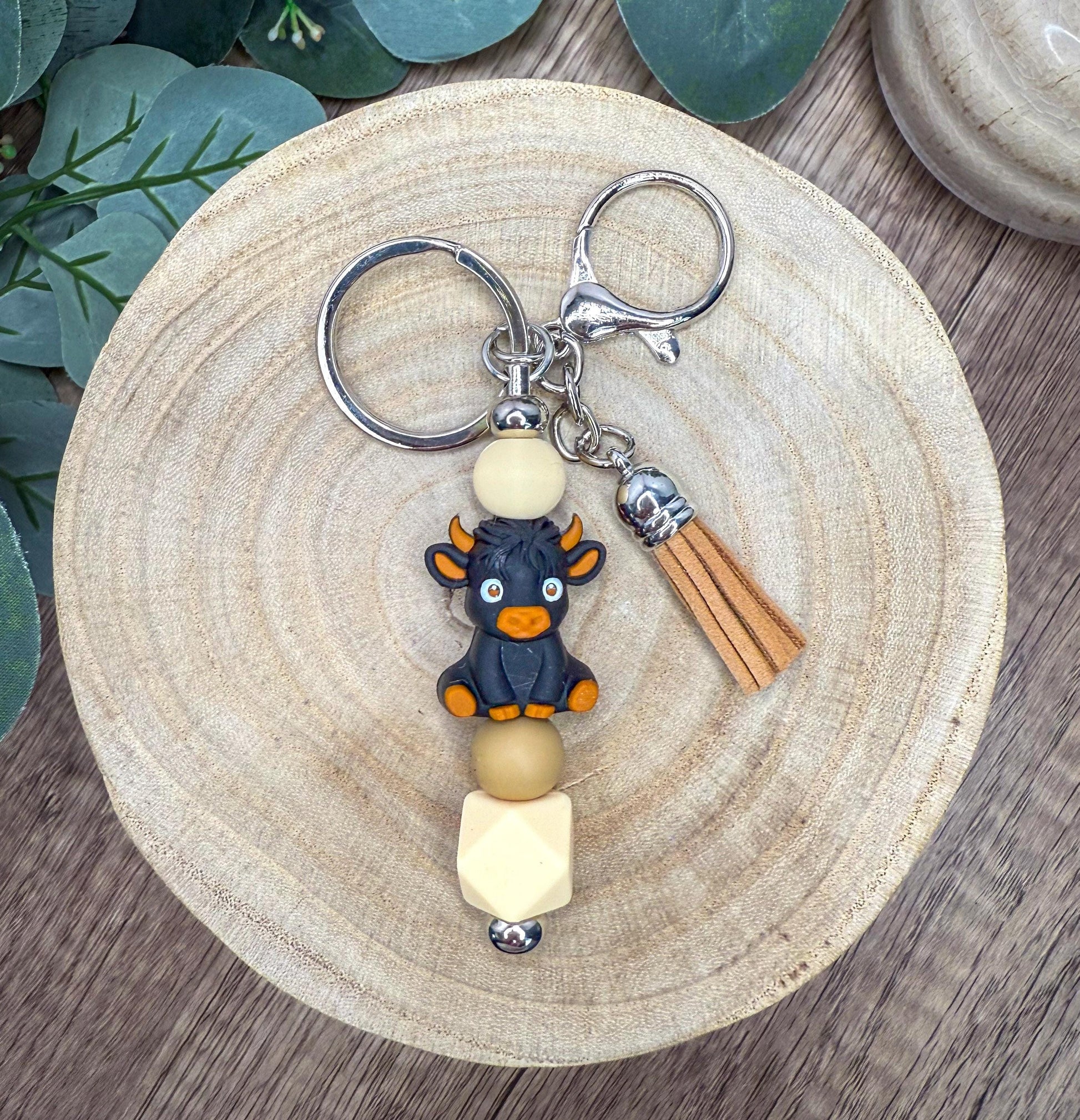 A keychain with a small black bull figurine and beige bead accents, placed on a wooden surface.