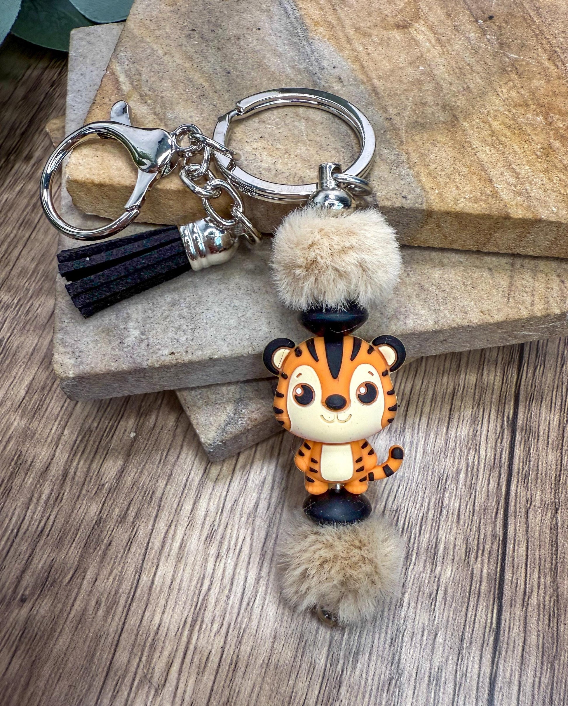 A keychain featuring a small tiger figurine with a fluffy pom pom attached to it.