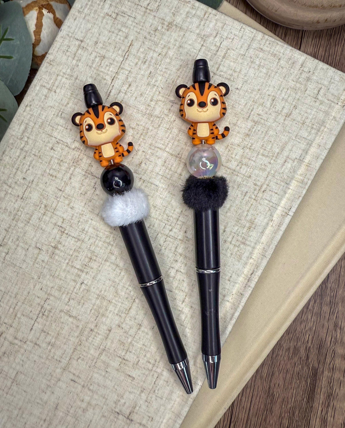 two pens with tiger figurines on them, placed on a textured surface.