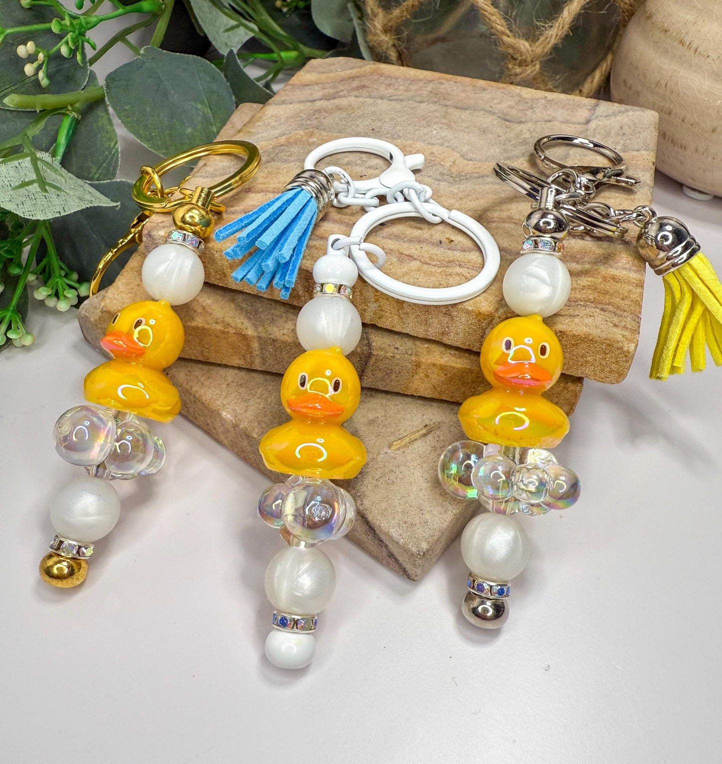 A set of colorful keychains with rubber duck designs, featuring yellow ducks and various decorative elements such as beads and tassels.