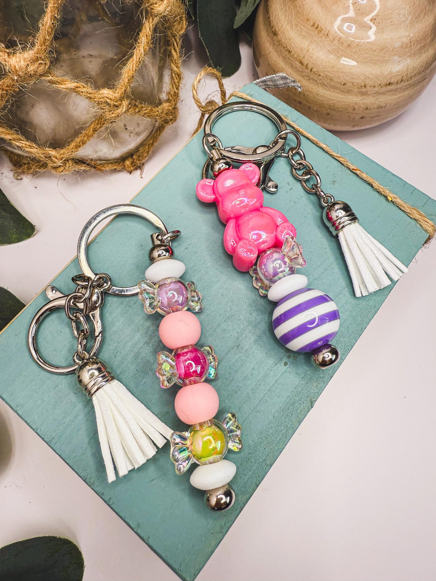 two colorful keychains with various charms, including a pink teddy bear, a purple and white striped bead, and a row of beads in different colors.