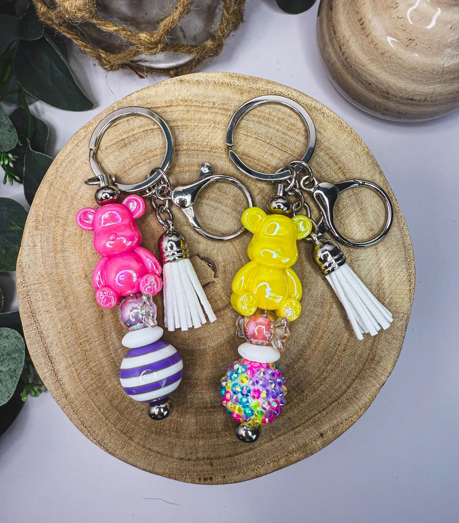 two keychains with colorful beads and tassels, one pink and one yellow, placed on a wooden surface.