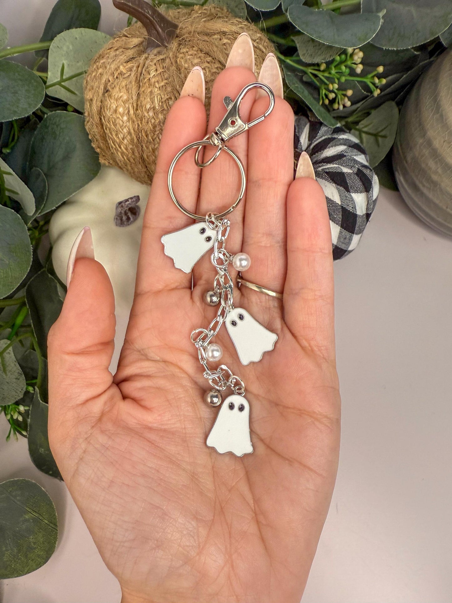 A hand holding a keychain with three small ghost-shaped charms attached to it.