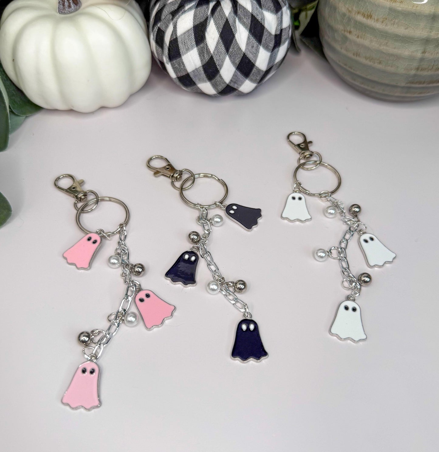 three keychains with ghost-like charms hanging from them, placed on a white surface.