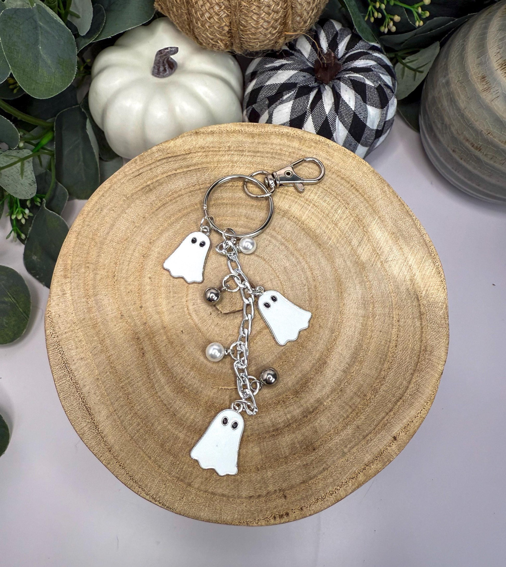 A wooden bowl with a keychain featuring ghost-shaped charms and silver bells.