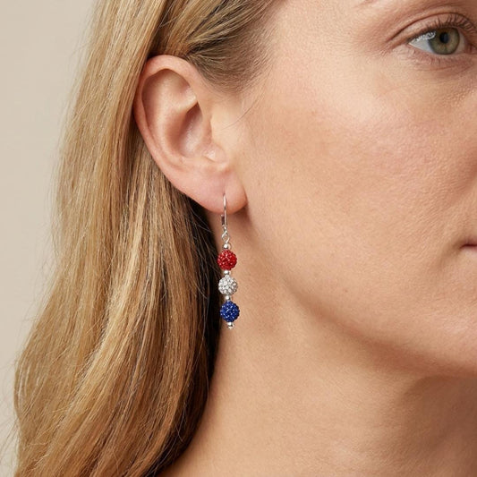 May include: Dangle earrings with red, silver, and blue beaded spheres. The earrings are suspended from silver-colored hooks. The red, white, and blue color scheme is a patriotic design. The earrings are a stylish accessory.
